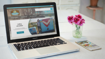 Laptop, phone, and a vase of magenta flowers on a white desk